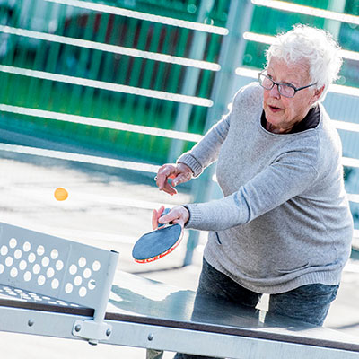 An elderly woman plays ping pong.